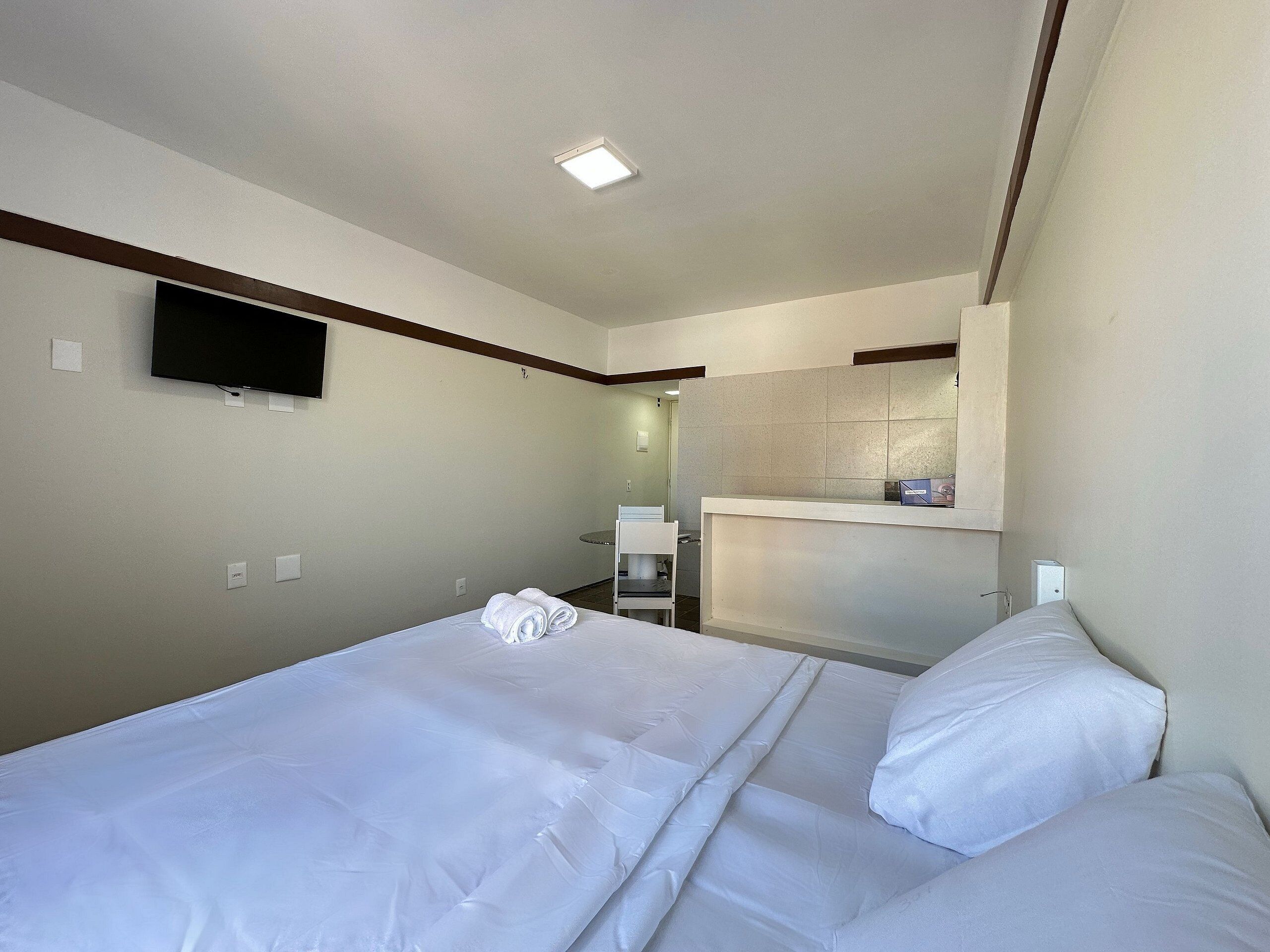 Ein Hotelzimmer mit einem Bett, einem an der Wand montierten Fernseher, einem kleinen Schreibtisch und einem Spiegel darüber.