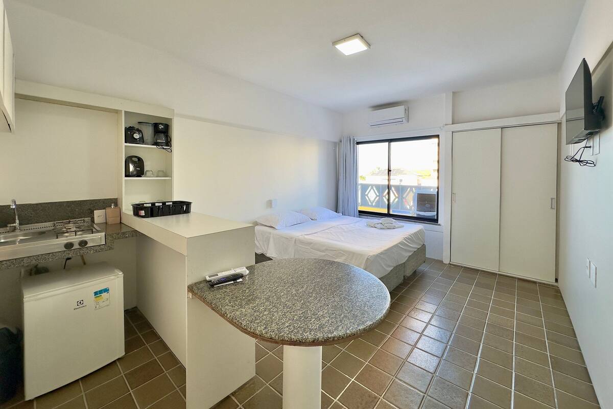 A compact hotel room with a kitchenette, a bed, a small dining table, and a window with a view.