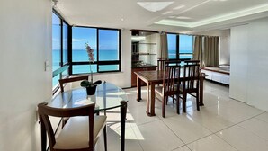 Una habitación de hotel con balcón, un área de comedor con una mesa de vidrio y una cama.