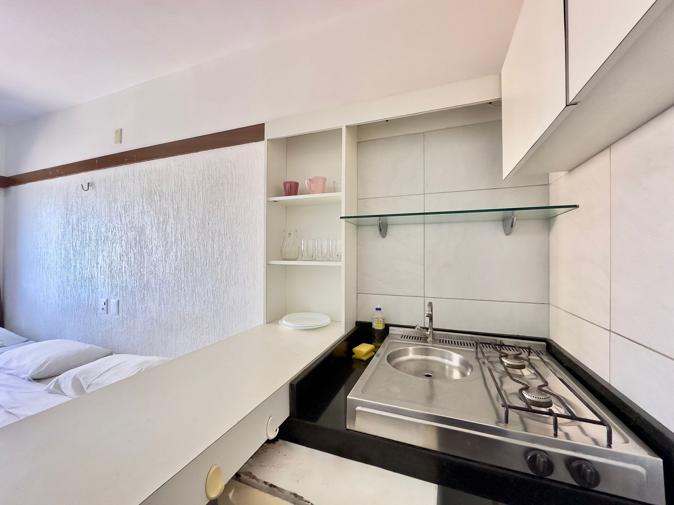 Uma cozinha compacta com fogão a gás, armários brancos e uma prateleira de vidro.