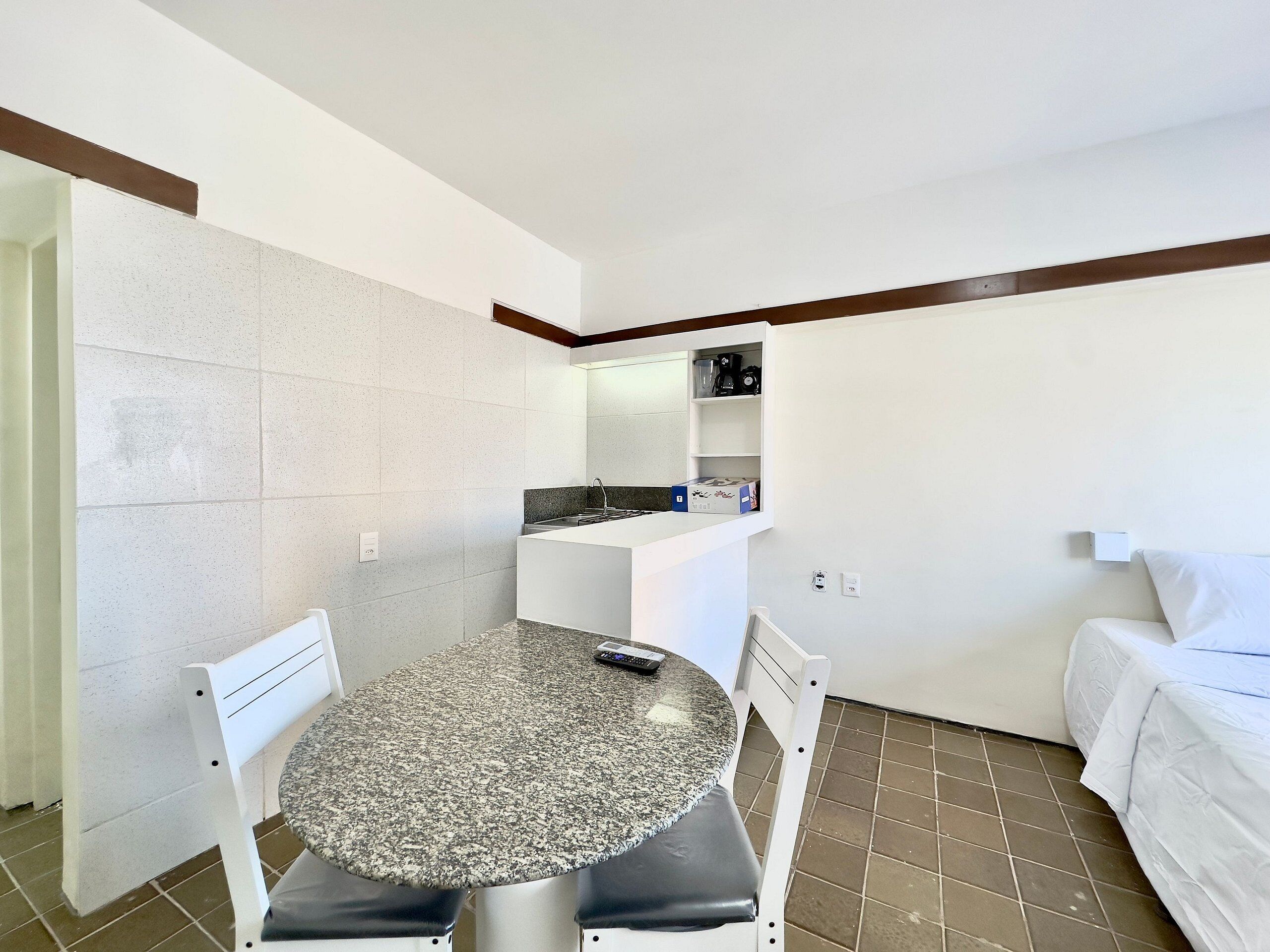 A compact room with a round table, two chairs, a bed, a kitchenette, and a small shelf.