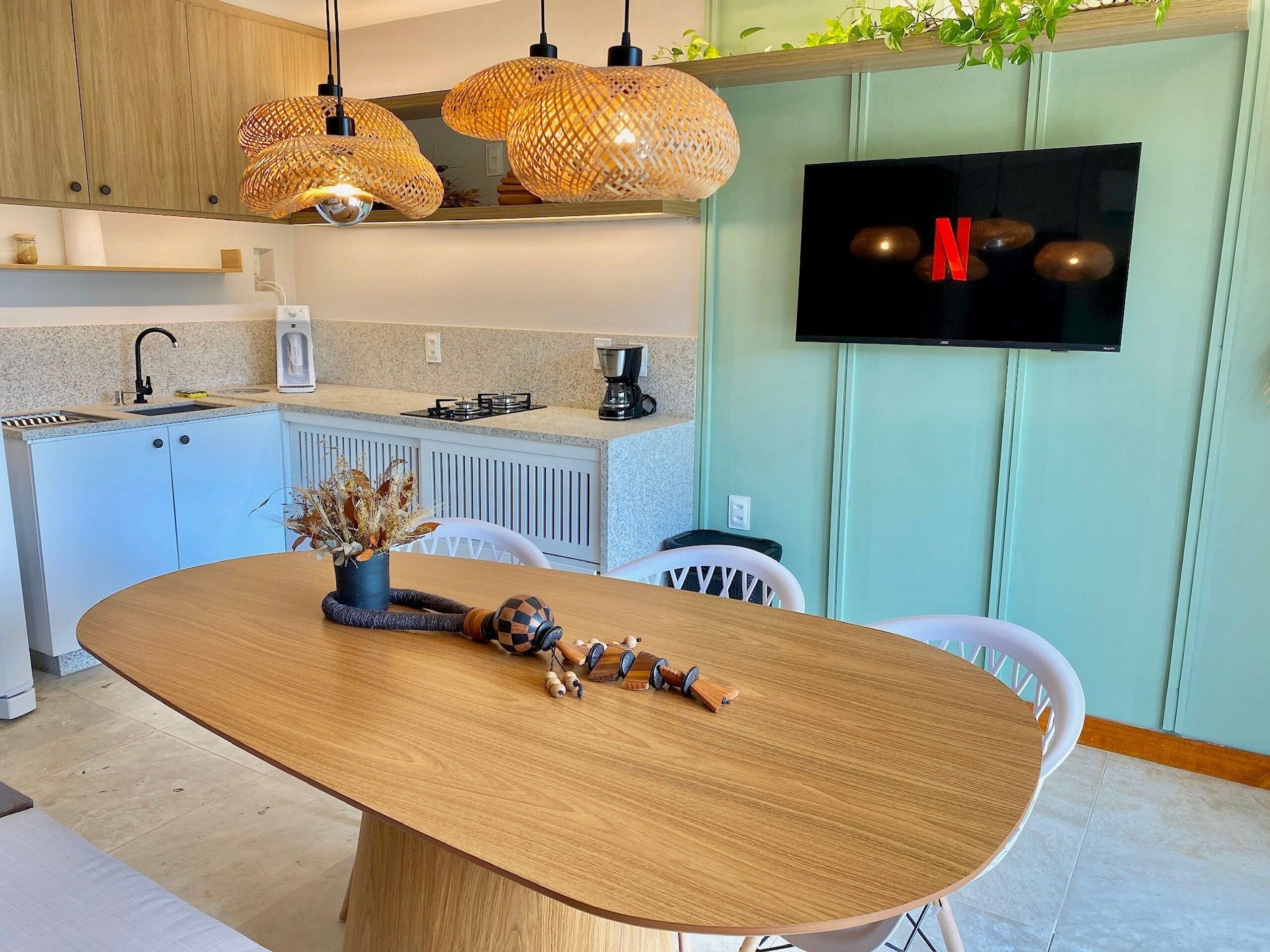 A modern kitchen with a dining table, wicker pendant lights, a TV, and a coffee machine.