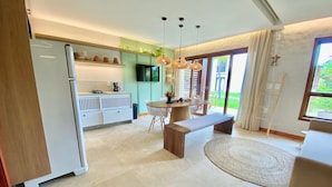 A modern kitchen with a built-in refrigerator, a dining area with a round table and bench, and a large window providing a view of the outdoors. - Taiba Beach Resort por Be My Guest! (São Gonçalo do Amarante)