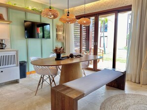 A modern dining area with a wooden table, white chairs, a bench, and a TV mounted on the wall. - Taiba Beach Resort por Be My Guest! (São Gonçalo do Amarante)