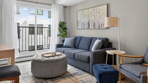 Ein modernes Wohnzimmer mit grauem Sofa, Hocker und Sessel, einem kleinen runden Tisch und einer Stehlampe.