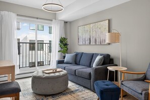 Ein modernes Wohnzimmer mit grauem Sofa, Hocker und Sessel, einem kleinen runden Tisch und einer Stehlampe.
