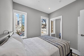 Ein Schlafzimmer mit einem Bett, einem Schreibtisch und einem Fenster mit Blick auf die Stadt.