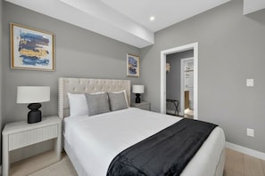 A bedroom with a large bed, two bedside tables, and artwork on the walls. - Luxury 2BR | Near Stampede | Modern | AC (Calgary)