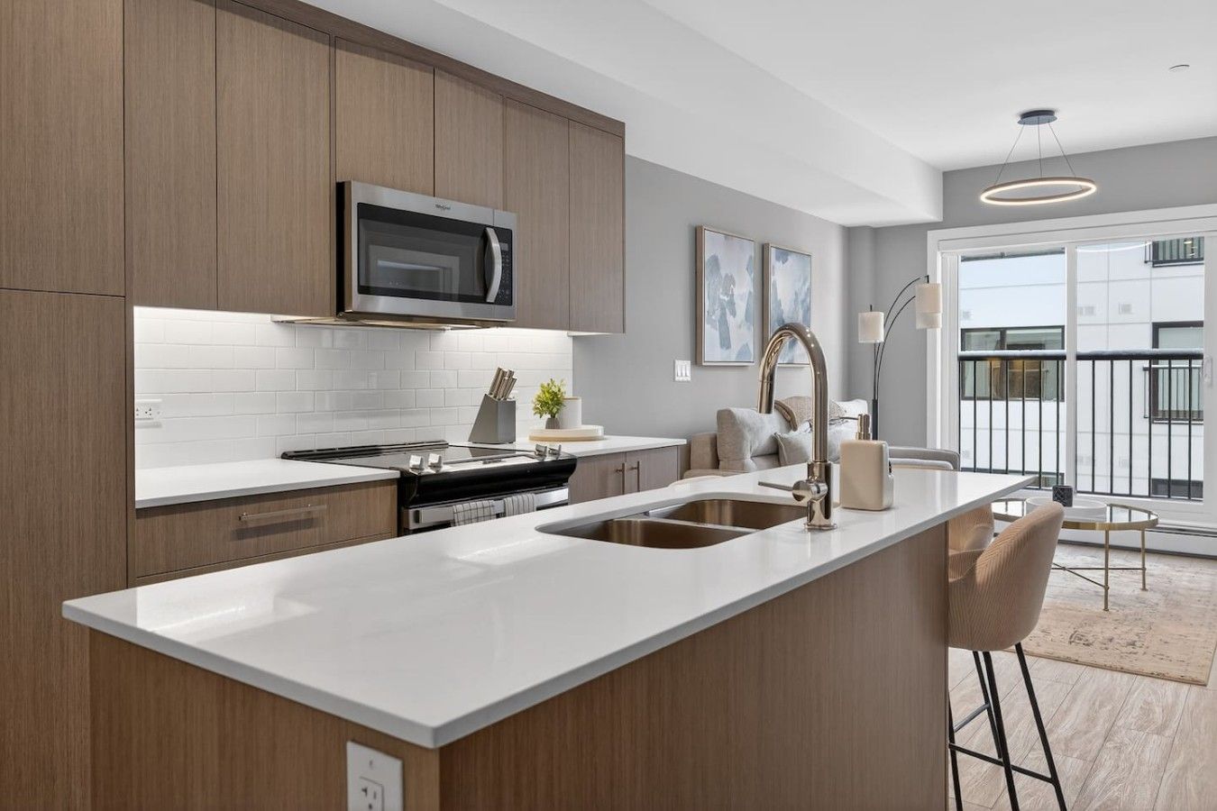 A modern kitchen with a stainless steel microwave, a double sink, and a large island with bar stools.