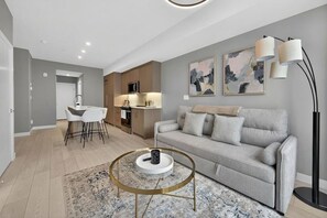 Ein modernes Wohnzimmer mit einem grauen Sofa, einem Couchtisch und einem Essbereich mit weißen Stühlen.