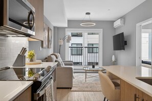 A modern kitchen with a built-in oven, a dining area with a round glass table, and a sofa. - Luxury 2BR | Near Stampede | Modern | AC (Calgary)