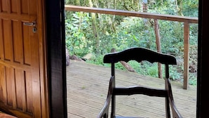 Une porte en bois, une chaise en osier et une vue sur une forêt par une grande fenêtre.