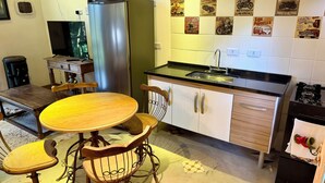 Une cuisine de taille réduite avec une table ronde en bois, deux chaises, un réfrigérateur en acier inoxydable, un évier et des placards.