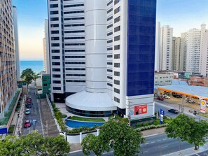 A modern high-rise building with a curved facade, a rooftop pool, and a visible Shell gas station. - Flat no Saint Martin (Fortaleza)