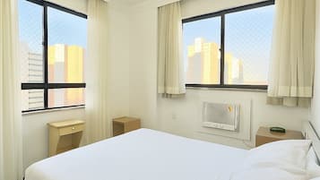 Una habitación de hotel con una cama grande, dos mesitas de noche, un calentador y una ventana con cortinas.