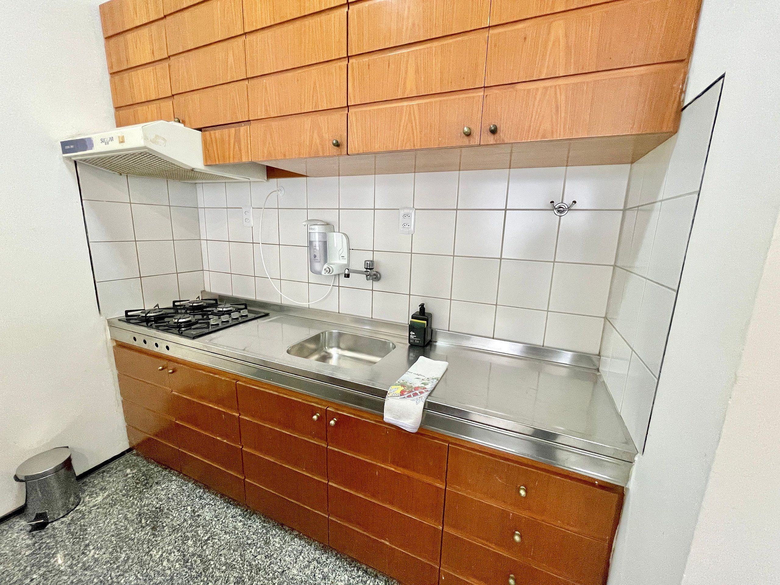 Cocina con estufa a gas, pileta de acero inoxidable, alacenas de madera y salpicadero de azulejos blancos.