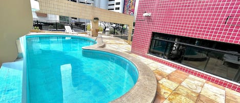 A swimming pool with a curved design, adjacent to a building with a red tiled exterior.