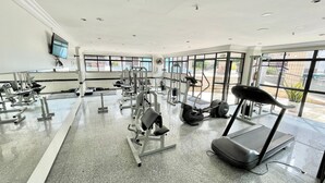 Un gimnasio con diversos equipos de ejercicio, amplias ventanas y suelo plano.