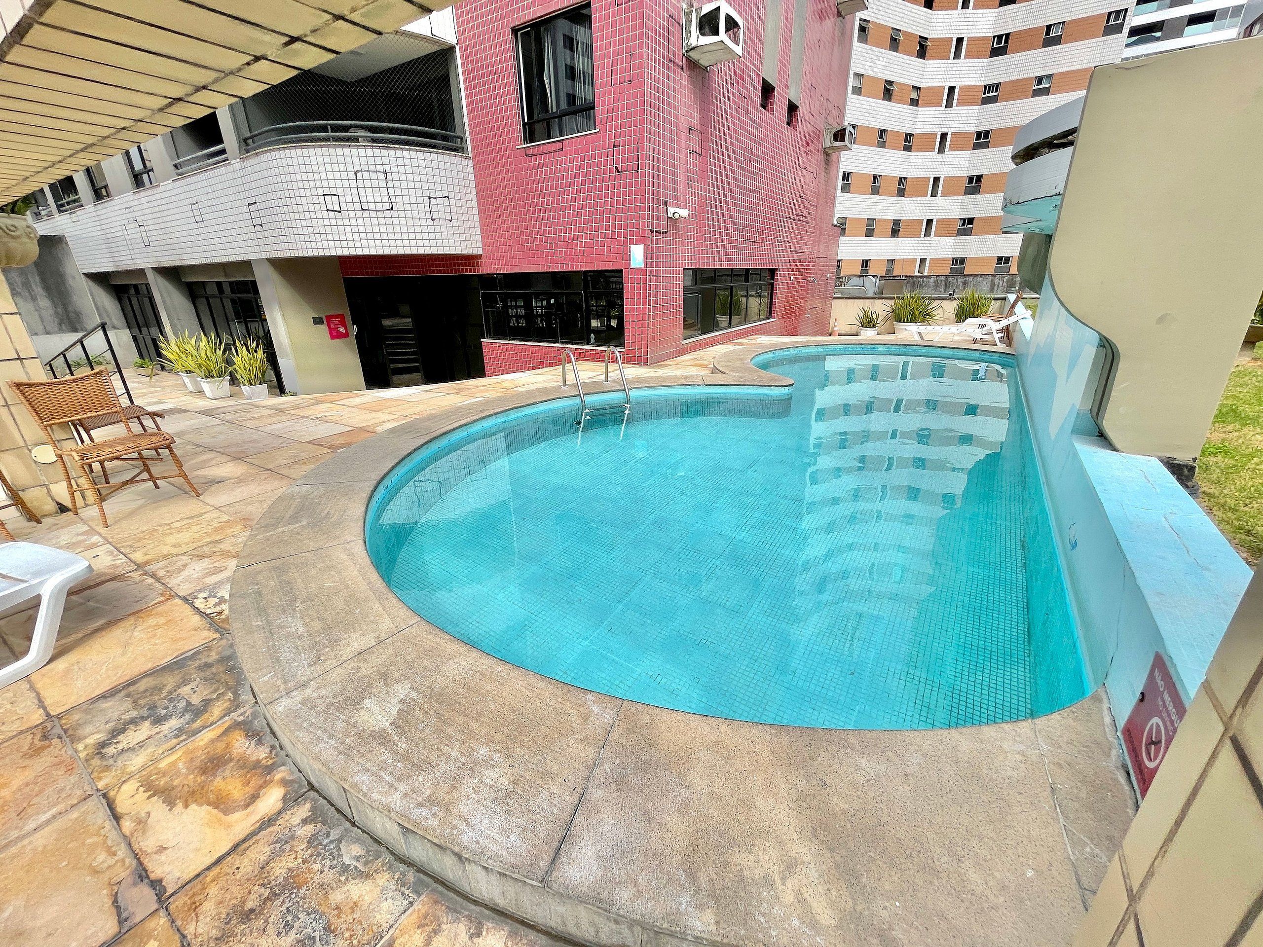 A swimming pool with a curved design, surrounded by stone tiles and a wicker chair.
