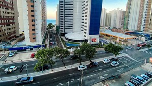 Calle urbana con edificios altos, múltiples carriles, coches aparcados y una estación de servicio.