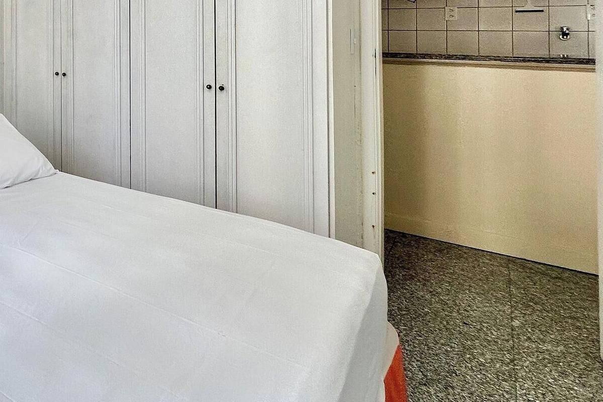 A single bed with white bedding in a room with white walls and a white wardrobe.