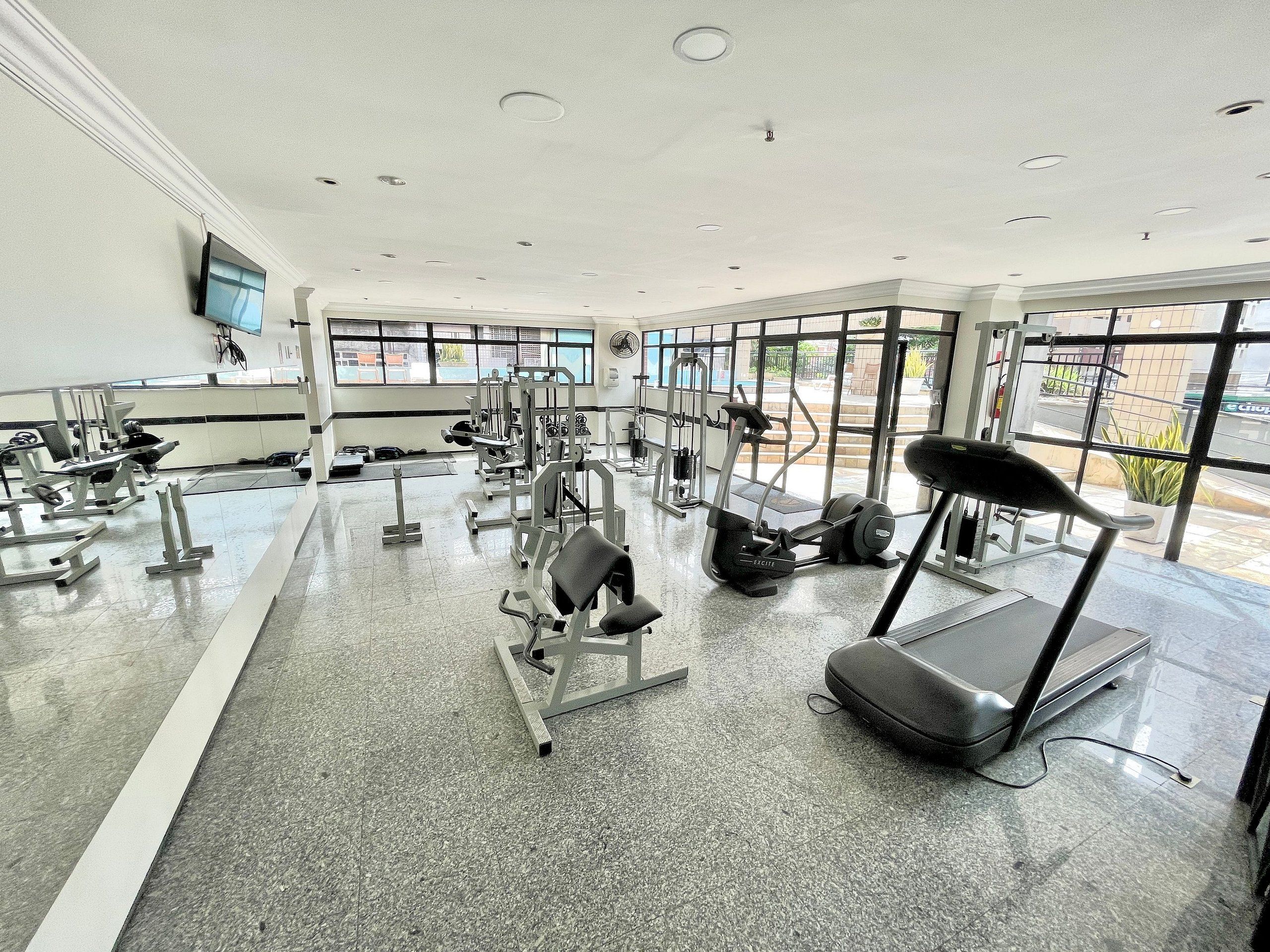 Uma academia com diversos equipamentos de exercício, amplas janelas e piso nivelado.