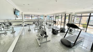 Uma academia com diversos equipamentos de exercício, amplas janelas e piso nivelado.