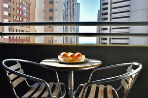 A balcony with a round table and two chairs, a bowl of fruit, and a cityscape view. - Flat no Saint Martin (Fortaleza)
