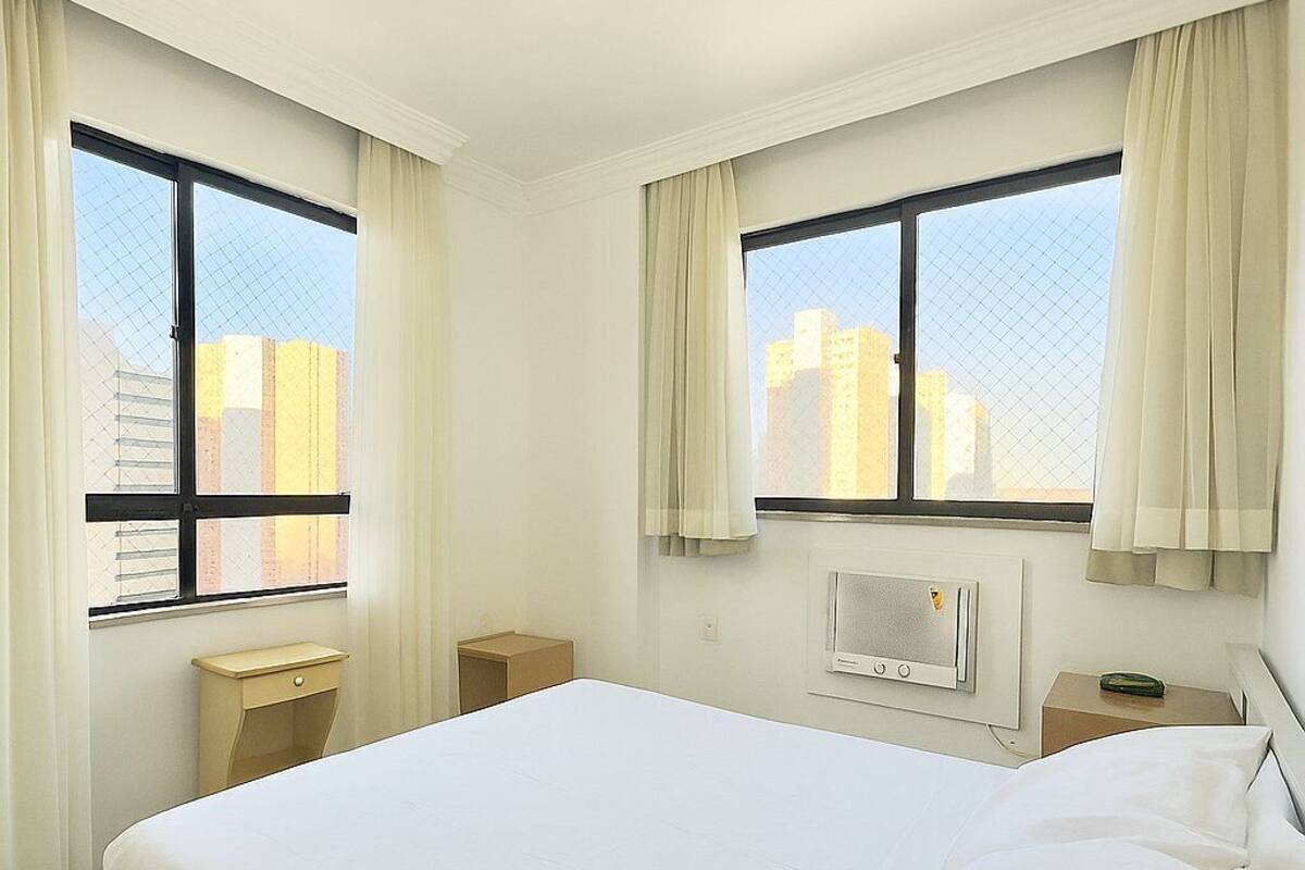 A hotel room with a large bed, two bedside tables, a heater, and a window with curtains.
