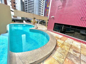 A swimming pool with a curved design, adjacent to a building with a red tiled exterior. - Flat no Saint Martin (Fortaleza)