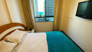 Quarto de hotel com cama, televisão, janela com cortinas e vista para edifícios.