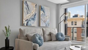 Un saló modern amb un sofà, coixins decoratius, una taula auxiliar amb una planta i obra d'art abstracta a la paret.