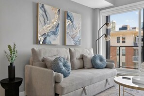 Ein modernes Wohnzimmer mit einer Couch, dekorativen Kissen, einem Beistelltisch mit Pflanze und abstrakter Wandkunst.