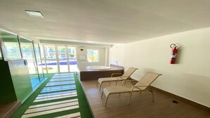 Een wachtruimte met een groen tapijt, een brandblusser aan de muur en een uitzicht op het buitenleven door grote ramen.