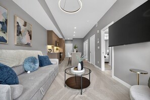 A modern living room with a grey sofa, a coffee table, and a flat-screen TV mounted on the wall. - Luxury 2 Bedroom | Min to Stampede | UG Prk | AC (Calgary)