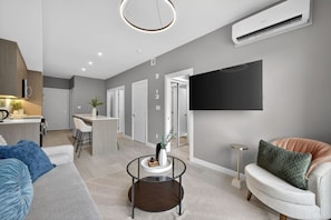 A modern living room with a sofa, coffee table, and a TV mounted on the wall. - Luxury 2 Bedroom | Min to Stampede | UG Prk | AC (Calgary)