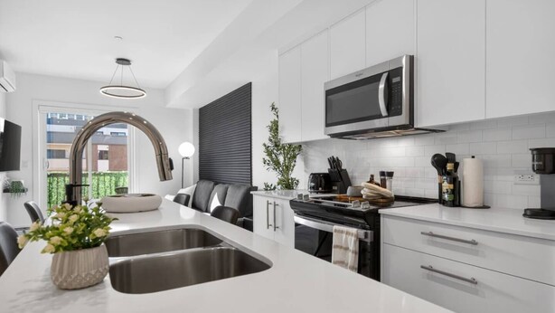A modern kitchen with a stainless steel sink, a built-in oven, and a microwave above the stove. - 2BR | DT | Balcony | AC | Mins to Saddledome (Calgary)
