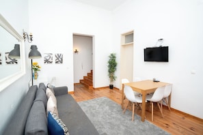 A compact living space with a sofa, dining table, chairs, a TV, and a staircase leading to another room. - Large 3-Bedroom 2 Bathroom Apartment, Multiple Bathrooms, Prime Lisbon Location (Lisboa)