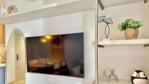A modern living room with a flat-screen TV mounted on the wall, a decorative plant, and a shelf with a unique design. - Vila Costeira - Beira Mar (Fortaleza)