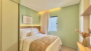 A bedroom with a bed, a window with curtains, a bedside table with a vase, and a wall-mounted artwork. - Vila Costeira - Beira Mar (Fortaleza)