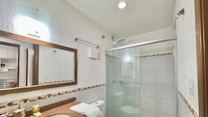 Een badkamer met een grote spiegel, een douchecabine van glas, een wastafel met een handdoek en een toilet.