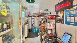 Een kleine buurtwinkel met schappen vol diverse producten, een koelvitrine en een digitaal bord.