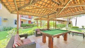 Een buitenzwembadgedeelte met een houten pergola, zitplaatsen en een pooltafel.