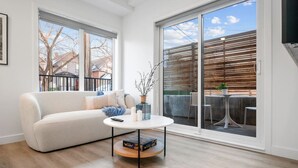 Sala de estar moderna com sofá, mesa de centro e vista para uma varanda com móveis de exterior.