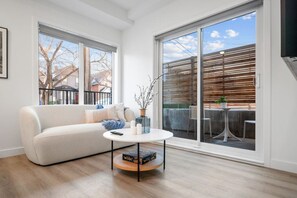Ein modernes Wohnzimmer mit Sofa, Couchtisch und Blick auf einen Balkon mit Gartenmöbeln.