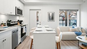Cozinha moderna com armários brancos, uma ilha central e uma área de jantar com mesa e cadeiras brancas.