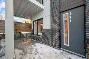 Ein modernes Gebäude mit einer dunkelgrauen Tür, einem sichtbaren Fenster und einem betonverlegten Untergrund mit Schnee.