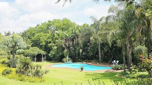 Una piscina rodeada de exuberante vegetación y un pequeño pabellón.