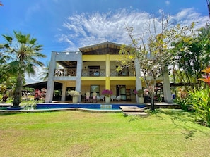 A two-story building with a pool, outdoor seating, and tropical landscaping.