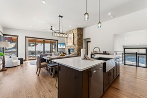 A modern kitchen with a large island, dining area, and a view of the outdoors. - Summit County Gem |  Designer Kitchen + Great Views (Silverthorne)